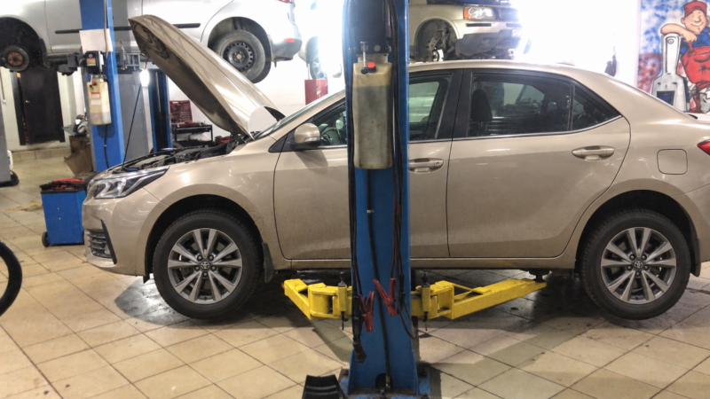 Бежевая Toyota Corolla с открытым капотом на подъёмнике в автосервисе
